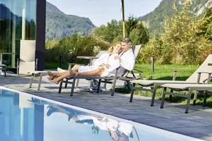 Paar in weißen Bademänteln liegt gemeinsam auf einer Sonnenliege am Outdoorpool des Hotel Oberstdorf