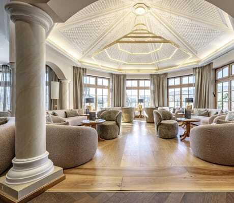 Loungebereich des Hotel Mooshof Wellness & Spa Resort mit mehreren Sesseln, Marmorsäulen und einer sehr imposanten, goldenen Lampe