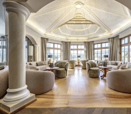 Loungebereich des Hotel Mooshof Wellness & Spa Resort mit mehreren Sesseln, Marmorsäulen und einer sehr imposanten, goldenen Lampe