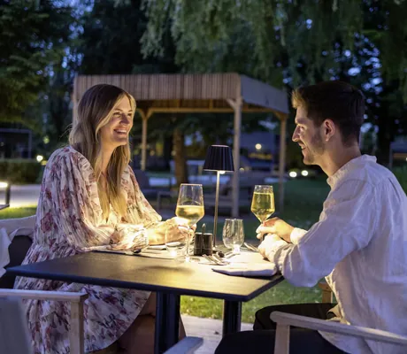blonde Frau und dunkelhaariger Mann sitzen auf der Outdoorterrasse des Das Parkhotel und trinken Weißwein