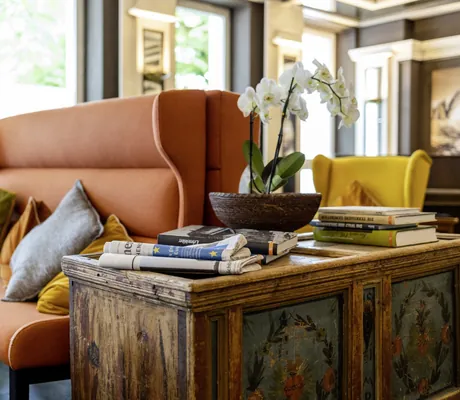 alte Bauerntruhe und modernes oranges Sitzsofa in der Lobby des Das Parkhotel