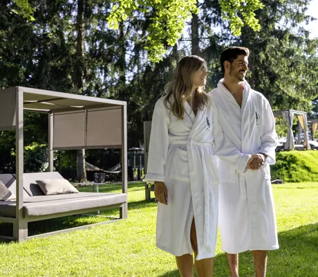 Paar mit weißen Bademänteln spaziert zwischen den Daybeds im Park des Das Parkhotel