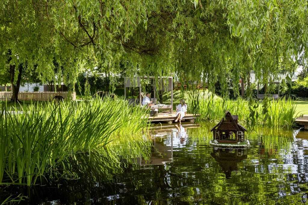 Paar in weißen Bademänteln auf dem Ponton am Naturteich des Das Parkhotel