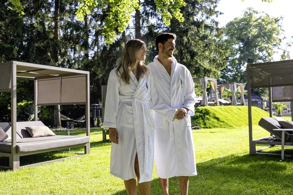 Paar in weißen Bademänteln schlendert durch den Park mit den Daybeds im Das Parkhotel