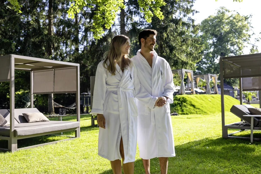 Paar in wei&szlig;en Badem&auml;nteln schlendert durch den Park mit den Daybeds im Das Parkhotel