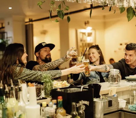 zwei Frauen und zwei Männer sitzen an der Bar des Beach Motel St. Peter-Ording und stoßen mit verschiedenen Drinks an