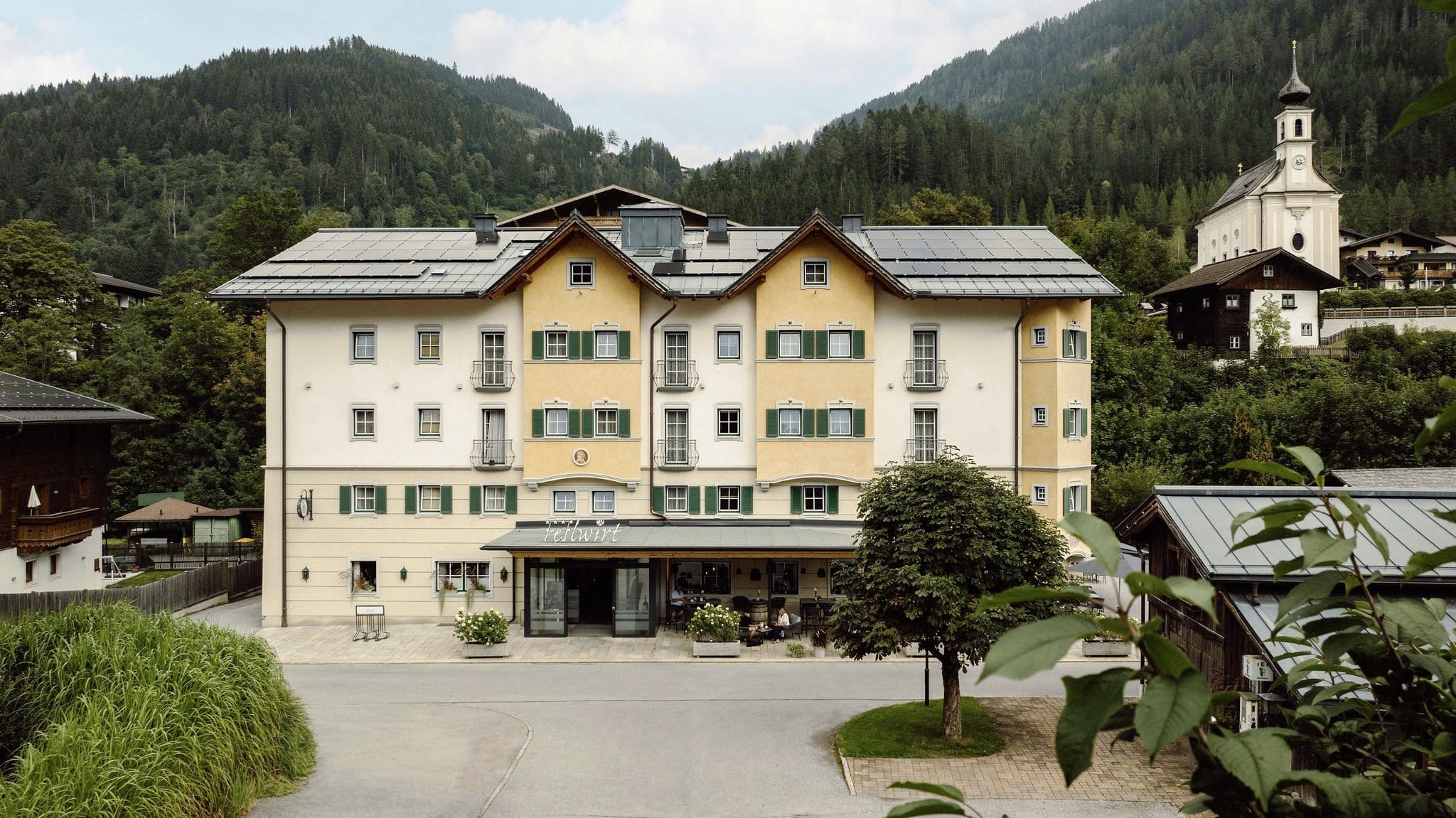 Fassade des RESL Resort im traditionellen Stil, eingebettet in eine malerische Berglandschaft und Kirche im Hintergrund