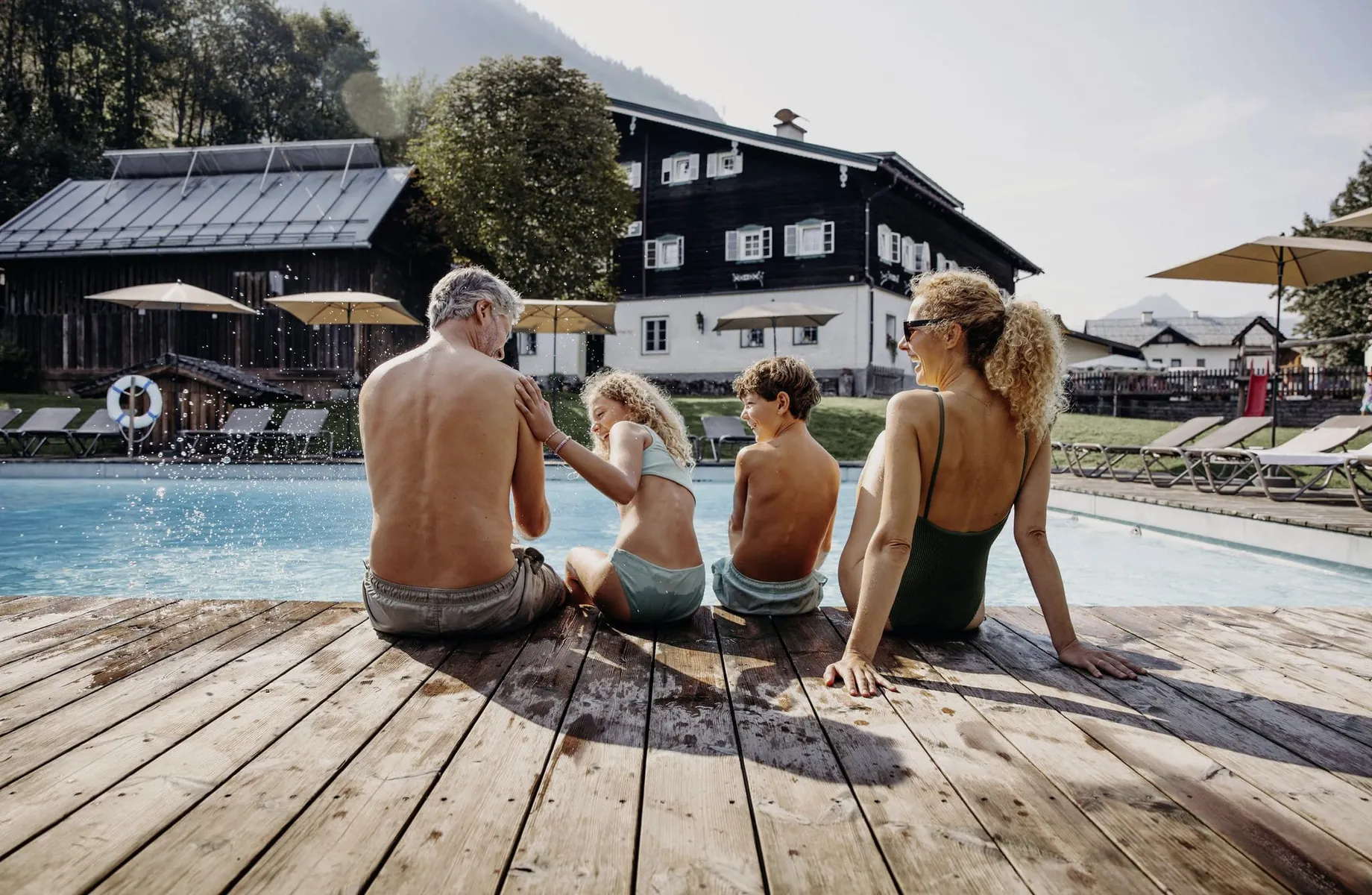 Familie mit zwei Kindern sitzt in Badekleidung am Beckenrand des Outdoorpool des Resl Resort