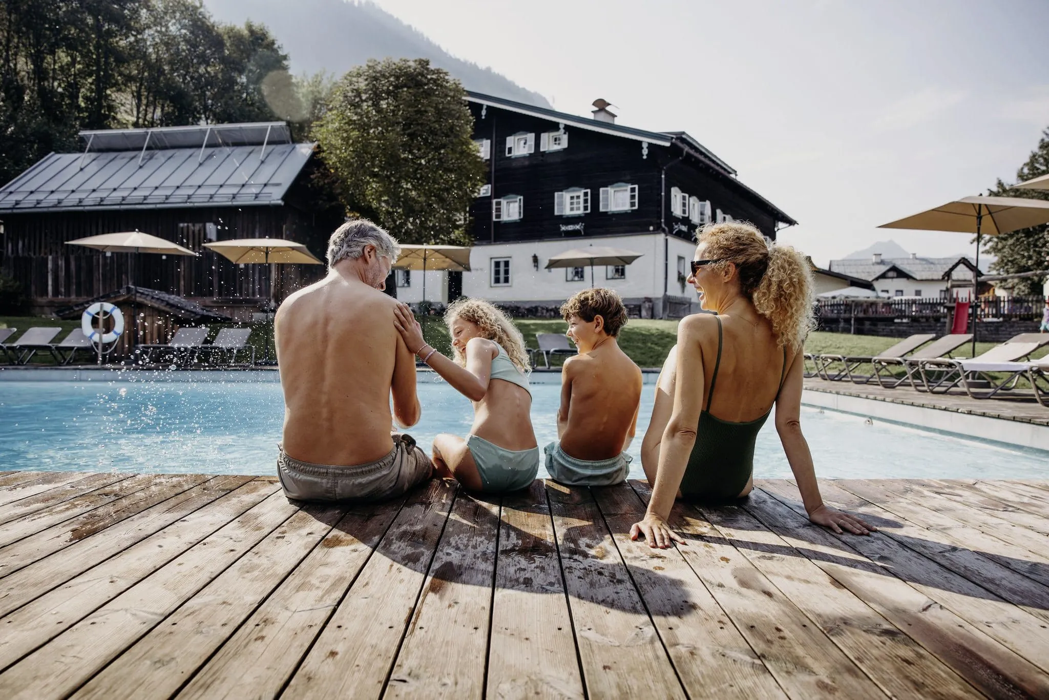 Familie mit zwei Kindern sitzt in Badekleidung am Beckenrand des Outdoorpool des Resl Resort