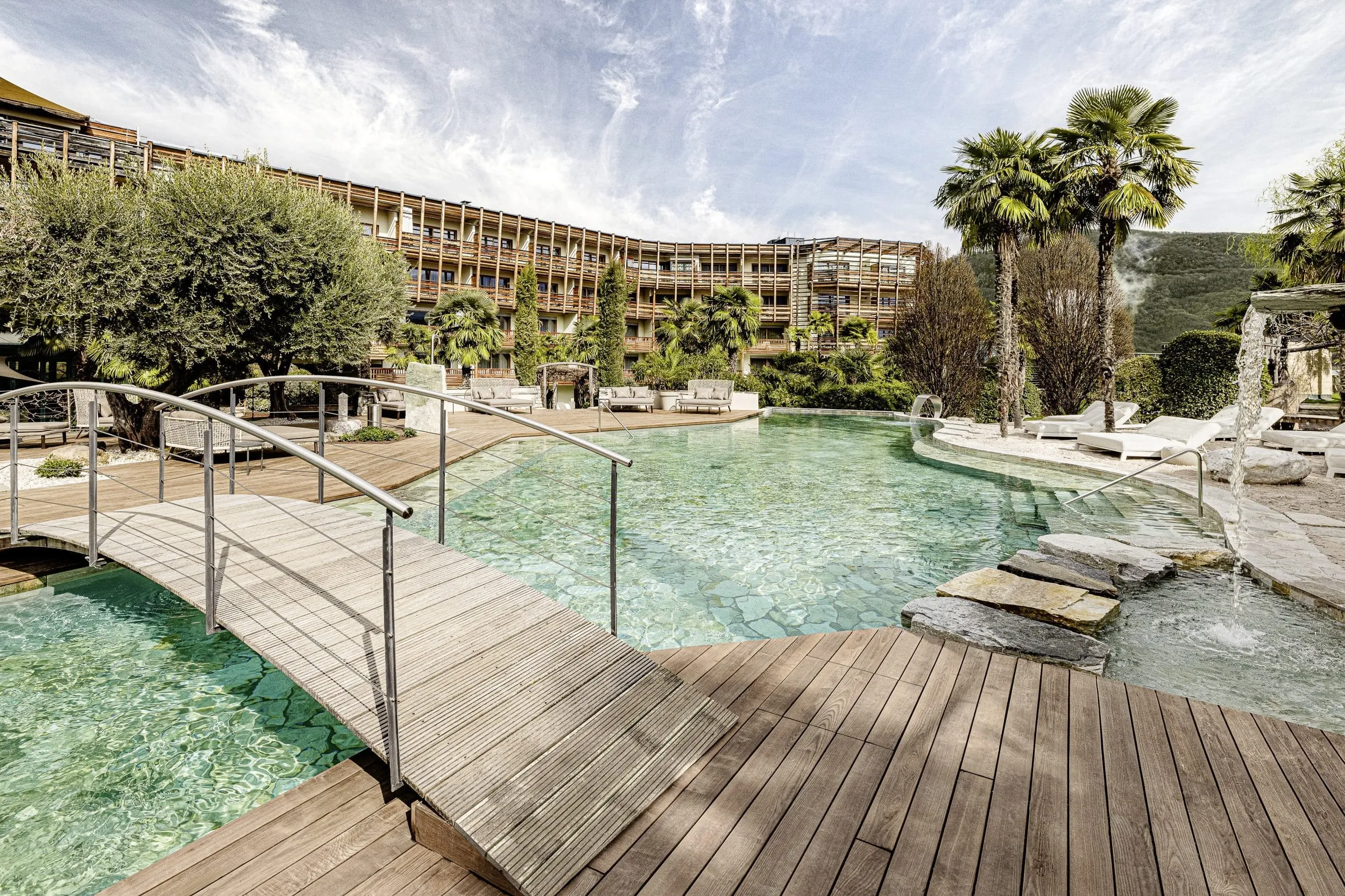 Naturbadeteich im SEELEITEN – Lake Spa Hotel mit Holzbrücke und Blick auf die Fassade