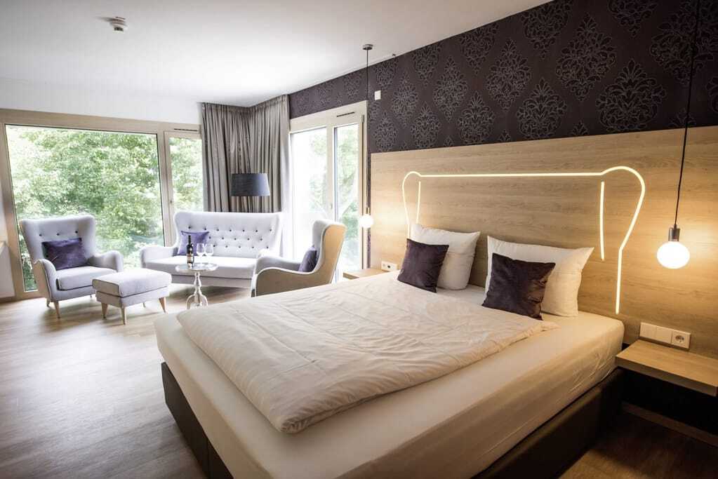 Doppelzimmer mit beleuchtetem Bettkopf und Loungemöbeln im Parkhotel Schillerhain