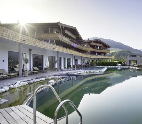 Blick auf die Fassade und den Naturbadeteich des Der Böglerhof – pure nature spa resort mit Bergpanorama im Hintergrund