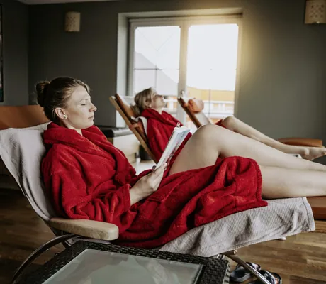 Frauen in roten Bademänteln entspannen auf Wellnessliegen im Ruheraum des Wellnesshotel Randsbergerhof