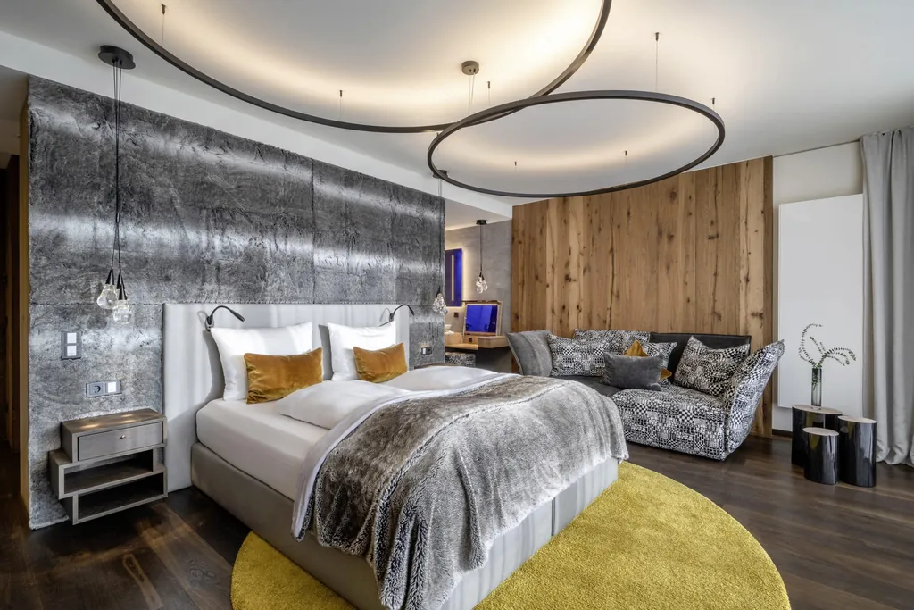 Doppelbett unter runden Bogenlampen mit grauem flauschigen Bettüberwurf und gelbem Teppich im Wellness- und Naturresort Reischlhof