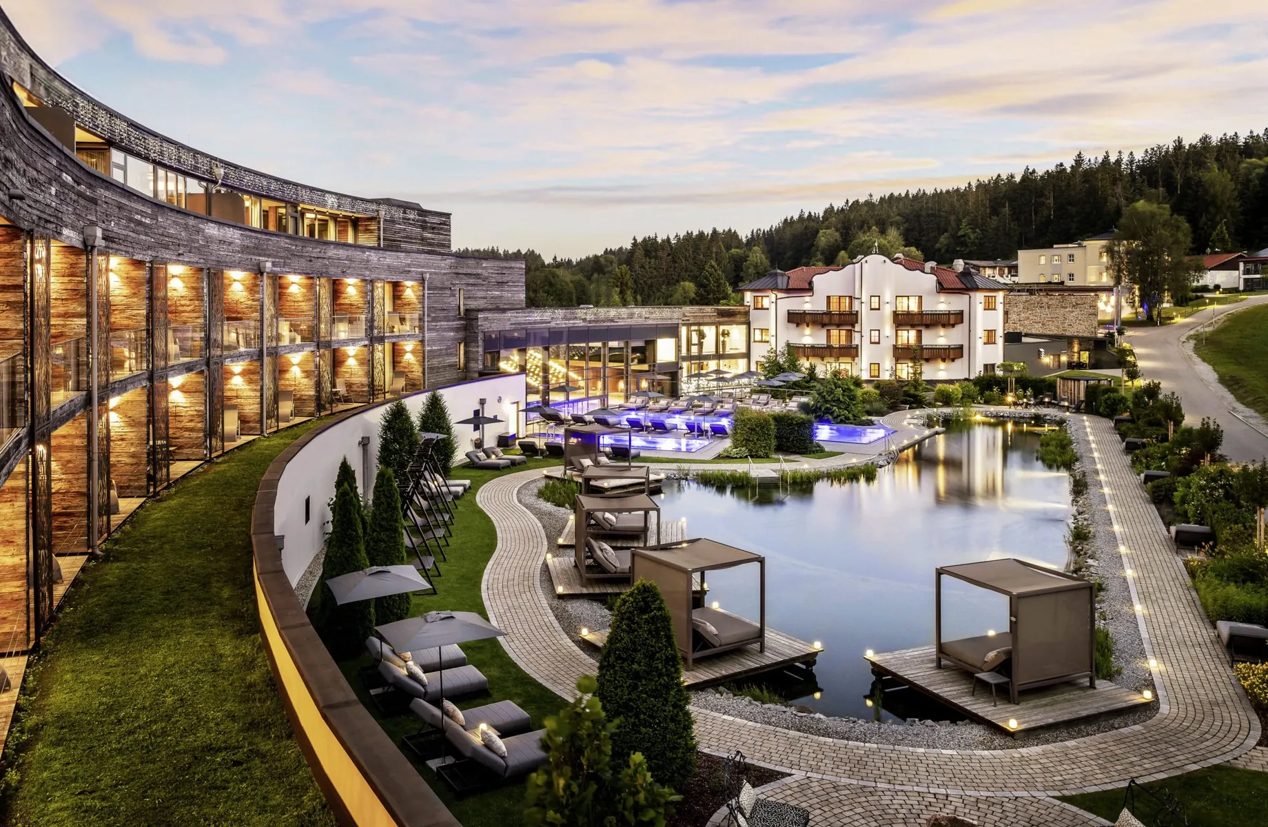 Außenansicht des Wellness-und Naturresort Reischlhof am Abend mit vielen Lichtern, Naturbadesee und einigen Daybeds