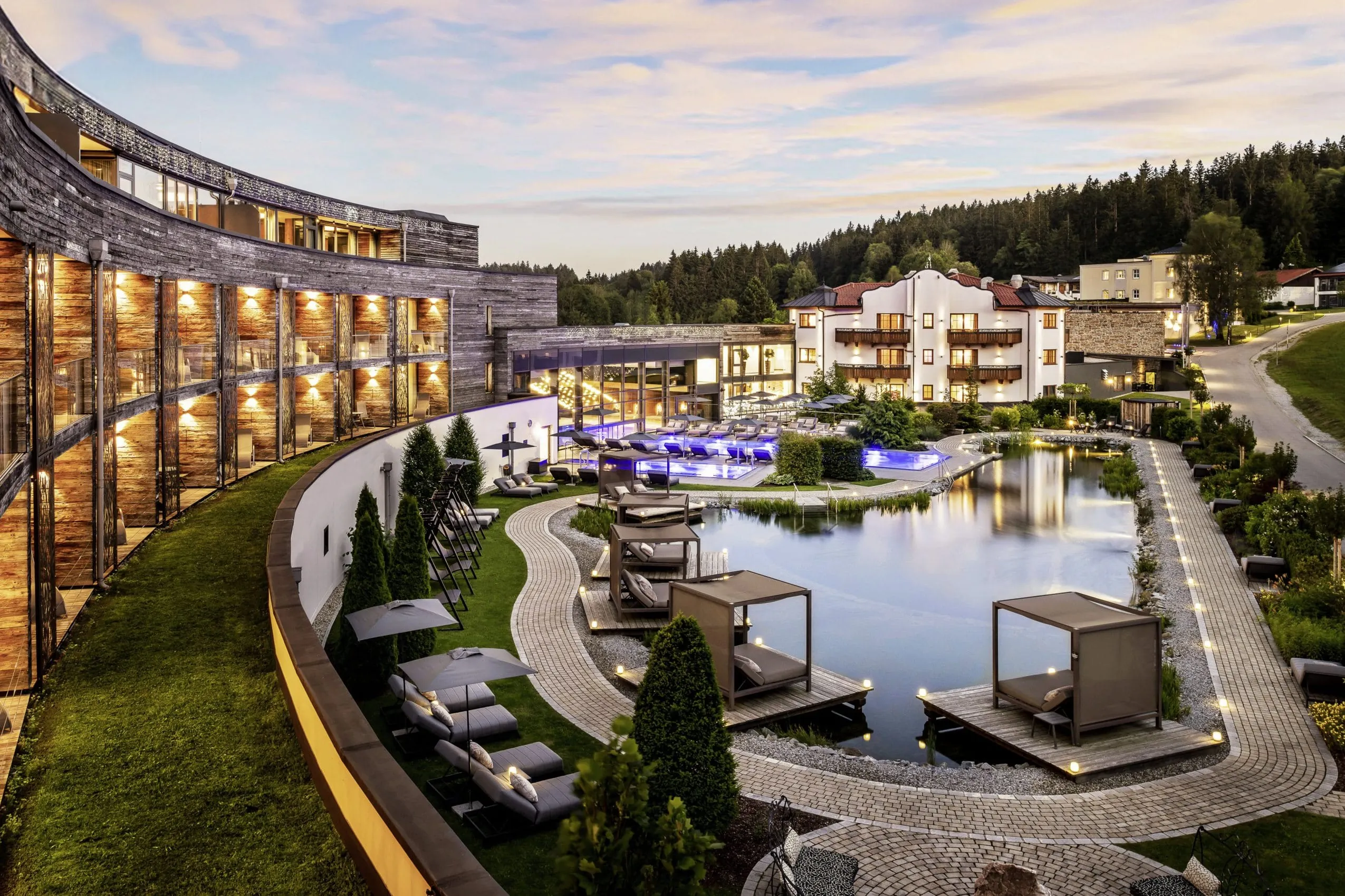 Außenansicht des Wellness-und Naturresort Reischlhof am Abend mit vielen Lichtern, Naturbadesee und einigen Daybeds