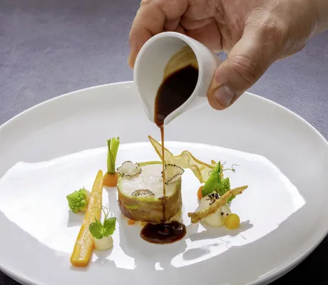 Hand gießt braune Soße auf eine schön angerichtete Speise im Wellness- und Naturresort Reischlhof