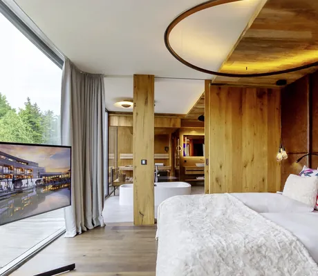 Luxuriöses Schlafzimmer der Sky-Suite im Wellness- und Naturresort Reischlhof mit Whirl-Badewanne und Sauna im Hintergrund