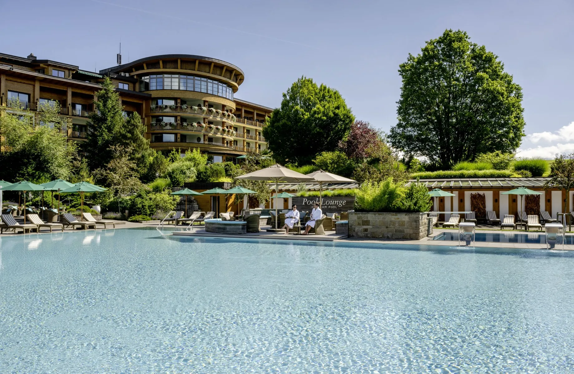 Paar in Bademänteln sitzt bei strahlendem Sonnenschein am Outdoorpool des Sonnenalp Resorts