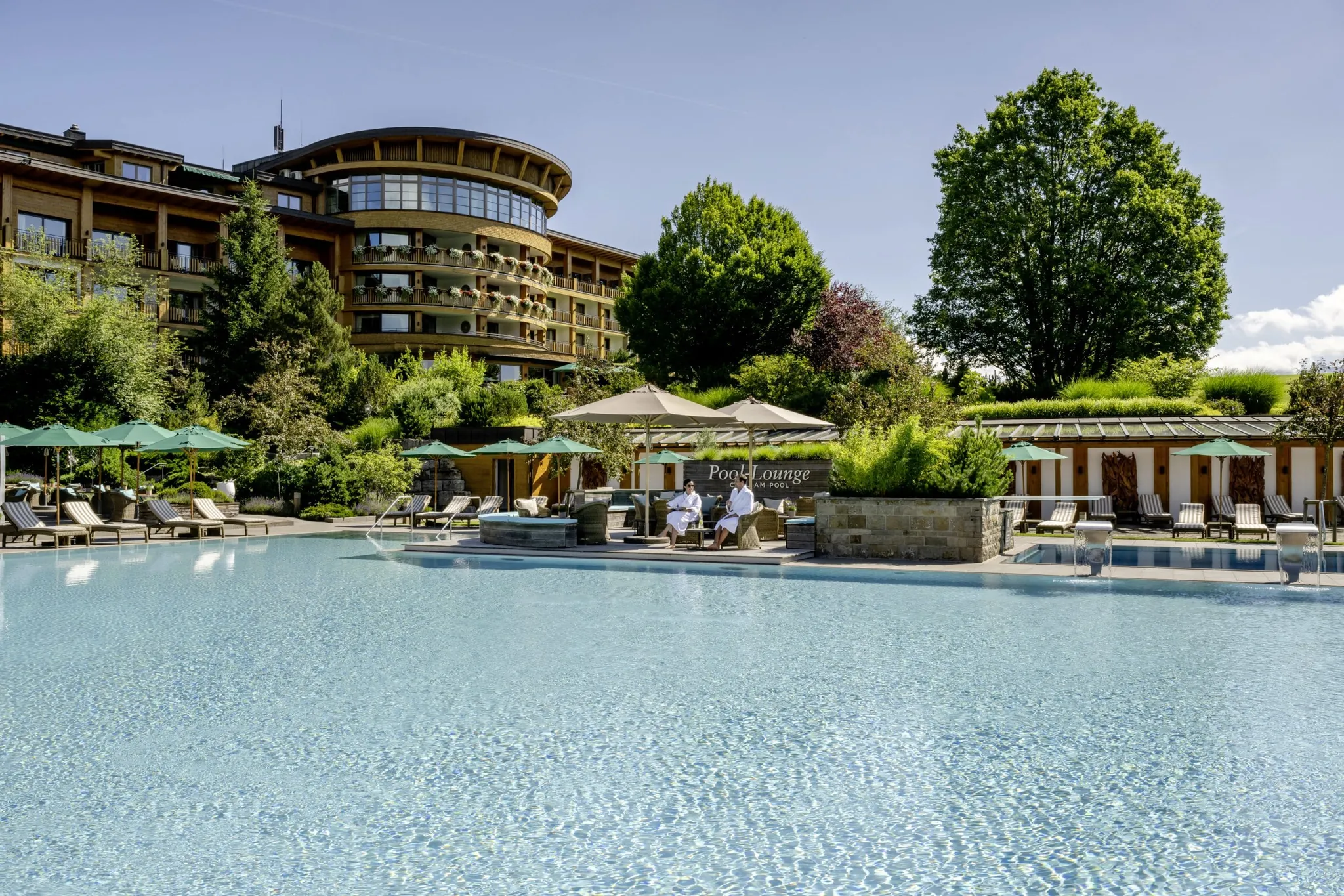 Paar in Bademänteln sitzt bei strahlendem Sonnenschein am Outdoorpool des Sonnenalp Resorts