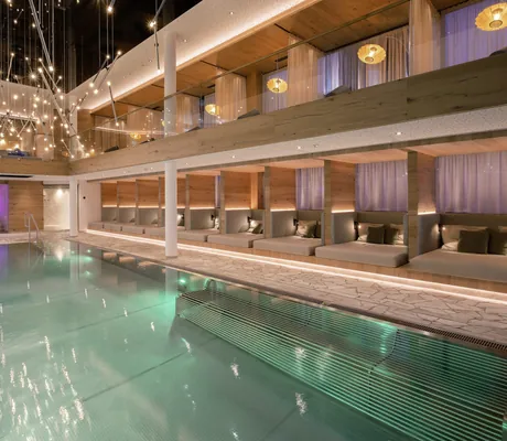 Eleganter Spa-Bereich mit grün beleuchtetem Indoorpool, stilvollen Liegen, moderner Lichtinstallation und Blick in die pink beleuchtete Sauna im Wellness & Naturhotel Tonihof****S