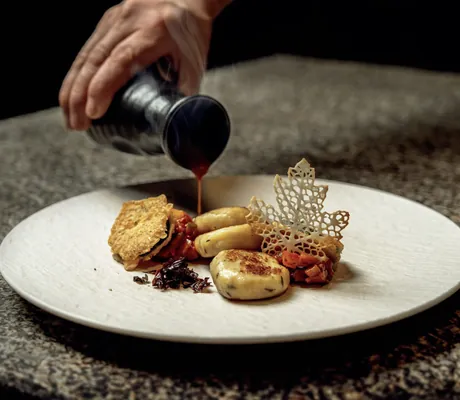 Hand gießt dunkle Soße auf ein schön angerichtetes Gericht im Wellness & Naturhotel Tonihof****S