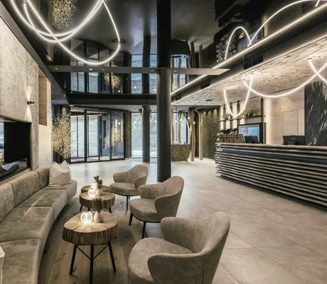 Moderner Lobbybereich des Wellness & Naturhotel Tonihof****S mit grauen Polstermöbeln und kleinen Holz-Beistelltischen, Mooswand und Baumstämme im Hintergrund