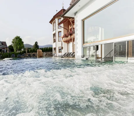 Sprudeliger Outdoorpool des Wellness & Naturhotel Tonihof****S mit Blick auf die Hotelfassade und Liegestühle am Beckenrand