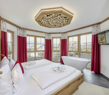Turmsuite des Wellness & Naturhotel Tonihof****S mit Doppelbett, freistehender Badewanne, roten Vorhängen, Holzdetails und langer, abgerundeter Fensterfront