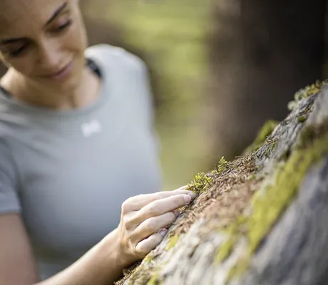 Frau legt ihre Hand auf einen mit Moos bewachsenen Baum in der Nähe des Hotel Winkler