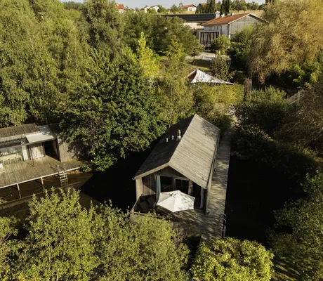 Luftaufnahme der Chalets des Hofgut Hafnerleiten mit Holzterrasse, Sonnenschirm, Liegestühlen, umgeben von dichtem Grün und Bäumen