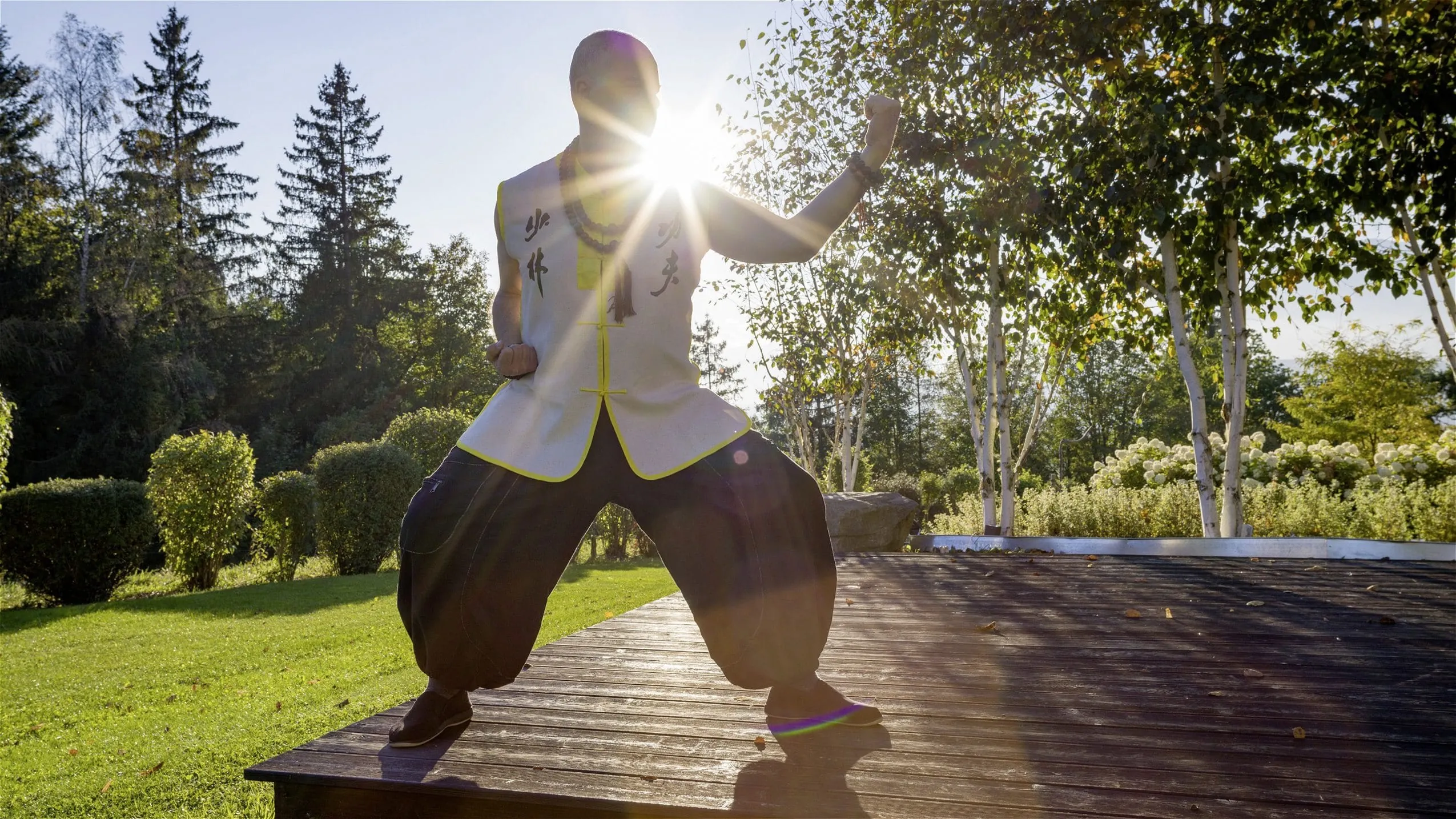 Mann steht in Tai Qi-Pose udn Kleidung auf der Holzterrasse des Panorama Royal