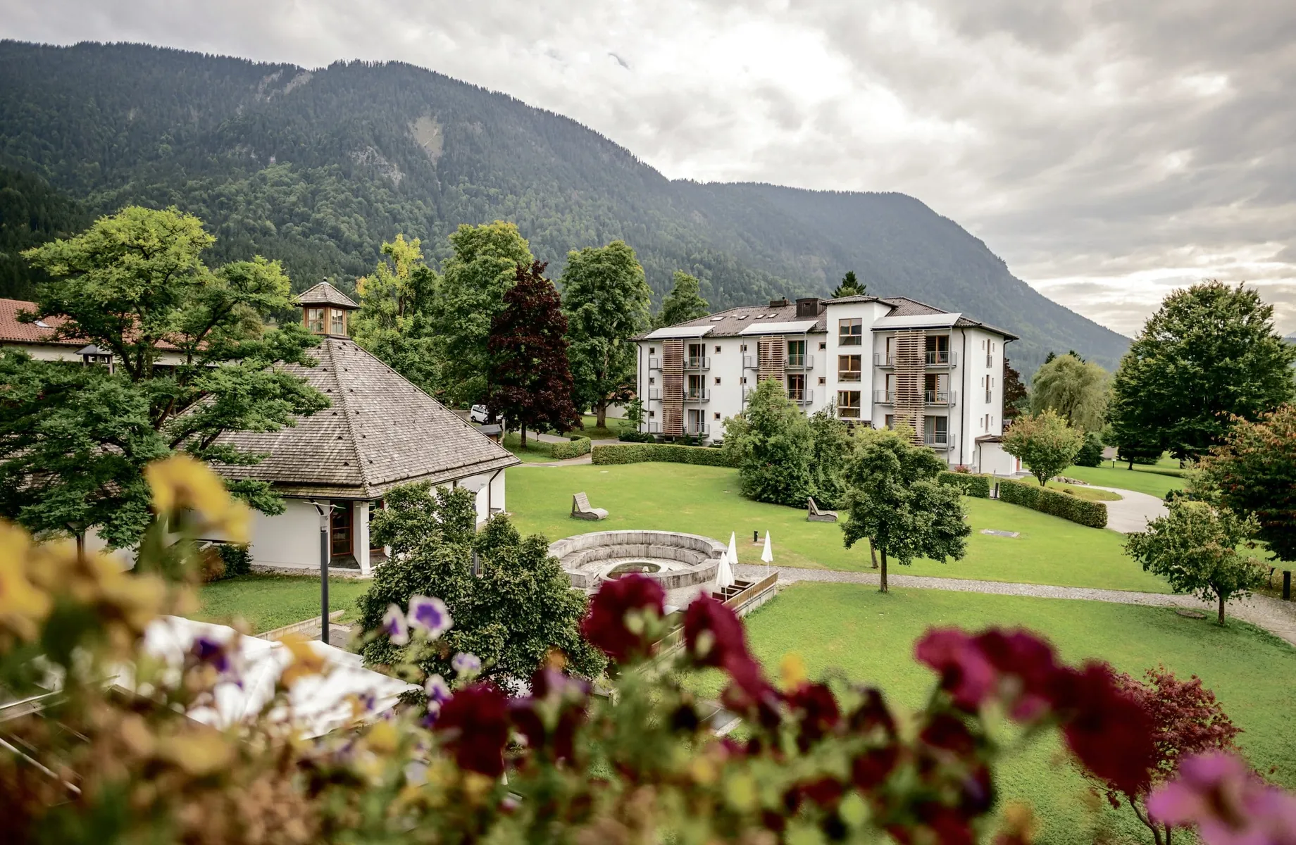 Hotelgebäude des Hotel Alpenblick Ohlstadt, eingebettet in die große Parklandschaft mit Kapelle