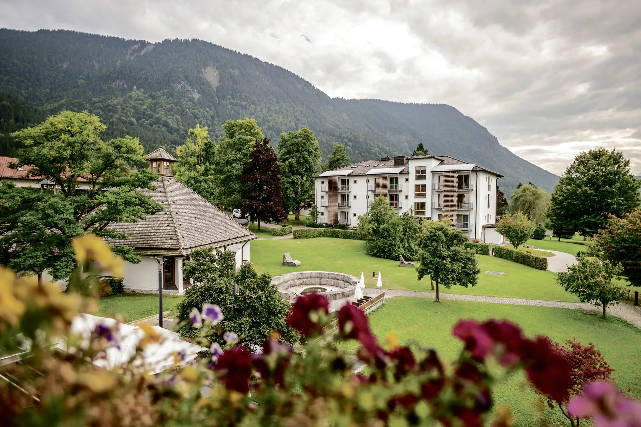 Hotelgebäude des Hotel Alpenblick Ohlstadt, eingebettet in die große Parklandschaft mit Kapelle