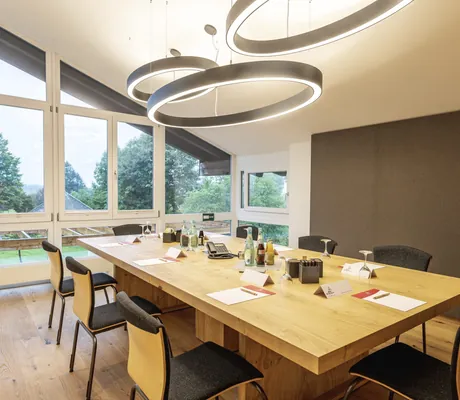 Besprechungsraum im Hotel Alpenblick Ohlstadt mit großem Holztisch und runden Deckenleuchten