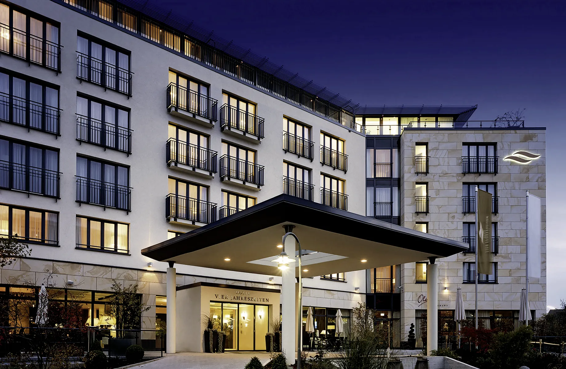 Beleuchtete Hotelfassade mit Balkonen und Eingangsbereich des Hotel Vier Jahreszeiten Starnberg bei Abenddämmerung