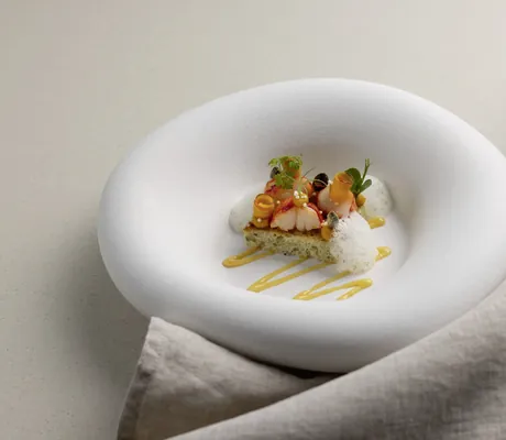 Fein angerichtetes Gourmetgericht des Gourmetrestaurants im Hotel Vier Jahreszeiten Starnberg mit glaciertem Hummer, Kräutern und Sauce auf weißem Teller mit breitem Rand