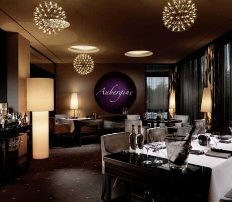 Elegantes Gourmetrestaurant "Aubergine" im Hotel Vier Jahreszeiten Starnberg mit stilvoll gedeckten Tischen, modernen Kugel-Lampen und gedämpfter Beleuchtung