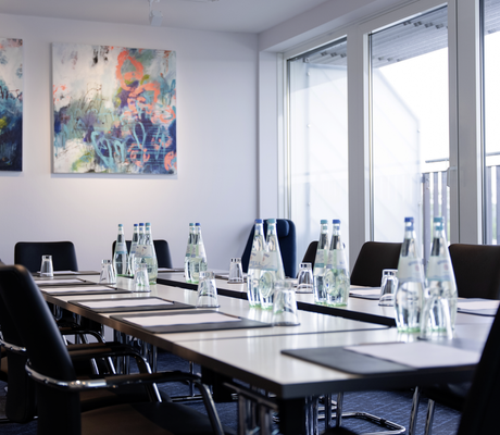 Tagungsraum "Franz" im Hotel Vier Jahreszeiten Starnberg mit langen Tischen, schwarzen Stühlen, Wasserflaschen, Gläsern und abstrakter Wandkunst