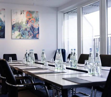 Tagungsraum "Franz" im Hotel Vier Jahreszeiten Starnberg mit langen Tischen, schwarzen Stühlen, Wasserflaschen, Gläsern und abstrakter Wandkunst