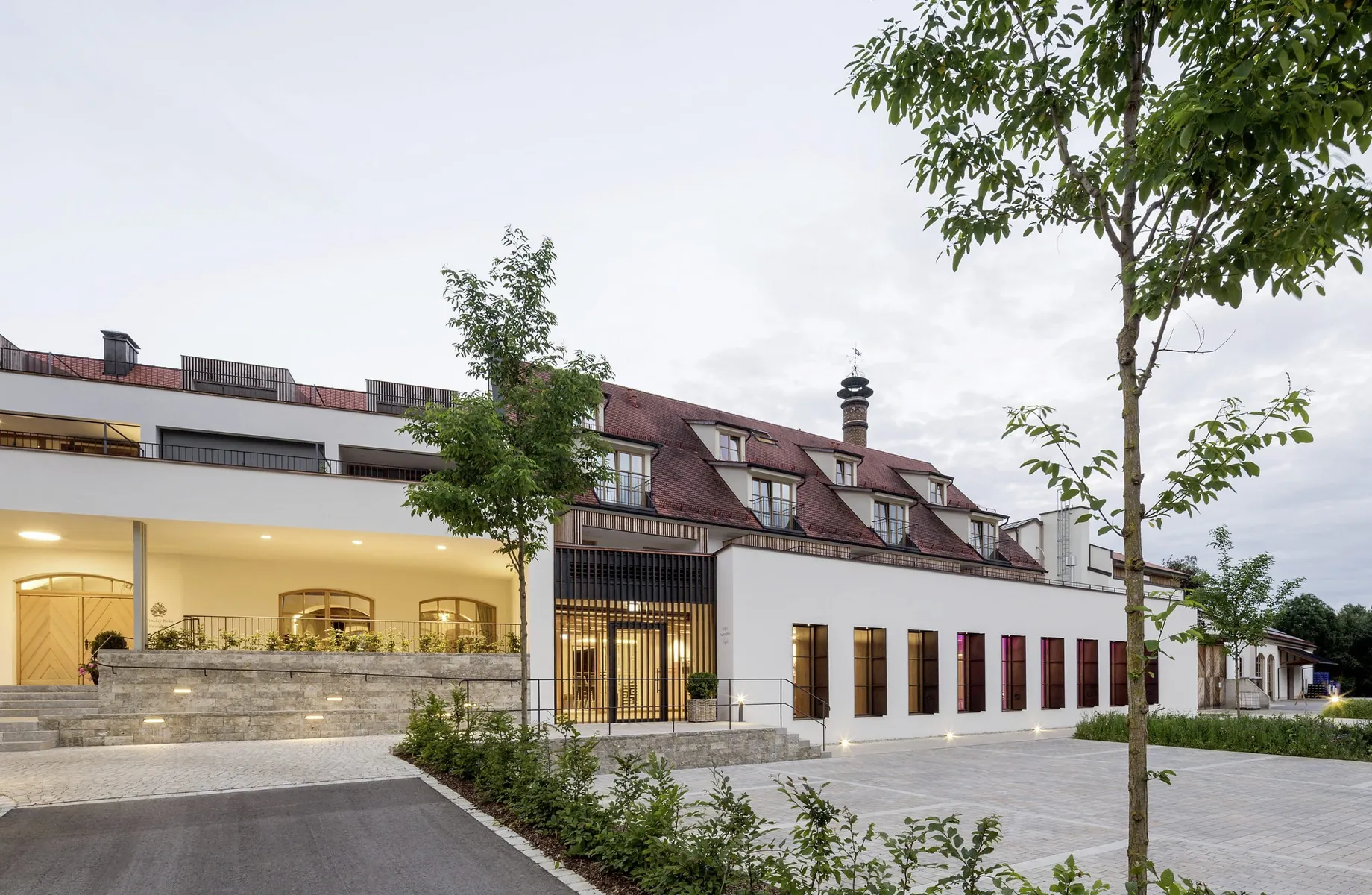 Beleuchtete Fassade mit rotem Ziegeldach und Parkplatz des Hotels Winkler Bräu
