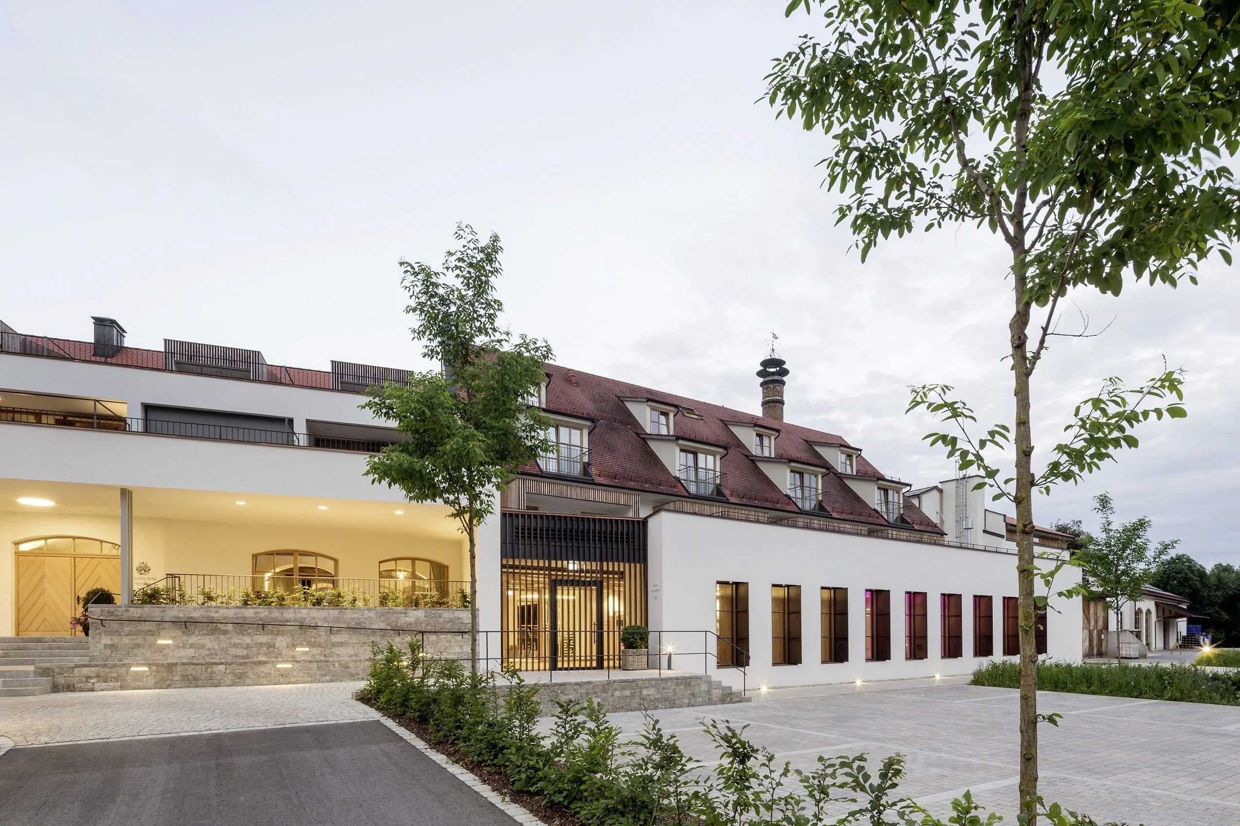 Beleuchtete Fassade mit rotem Ziegeldach und Parkplatz des Hotels Winkler Bräu