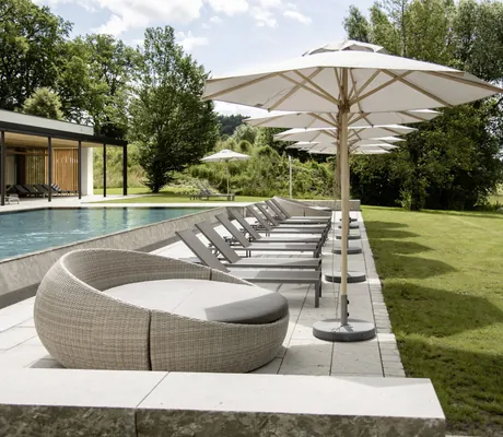 Outdoorpool des Hotel Winkler Bräu mit mehreren grauen Liegestühlen, weißen Sonnenschirmen und einer Liegewiese