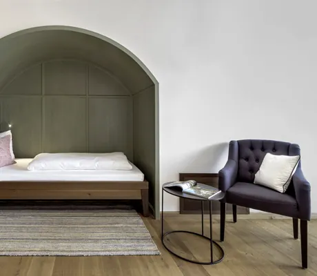 Gemütliche grün gestrichene Bettnische im Hotel Winkler Bräu mit rundem Beistelltisch davor und dunkelgrauem Sessel