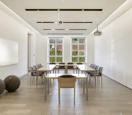 Heller Konferenzraum im Hotel Winkler Bräu mit Holz-Metall-Tischen, gepolsterten Stühlen, Whiteboard, Projektoren, Holzboden und großen Fenstern