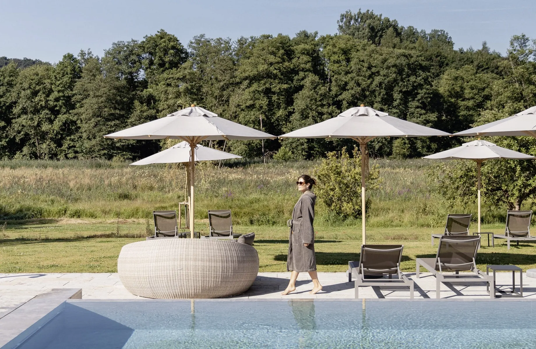 Frau in grauem Bademantel steht am Beckenrand des Outdoorpools des Hotel Winkler Bräu