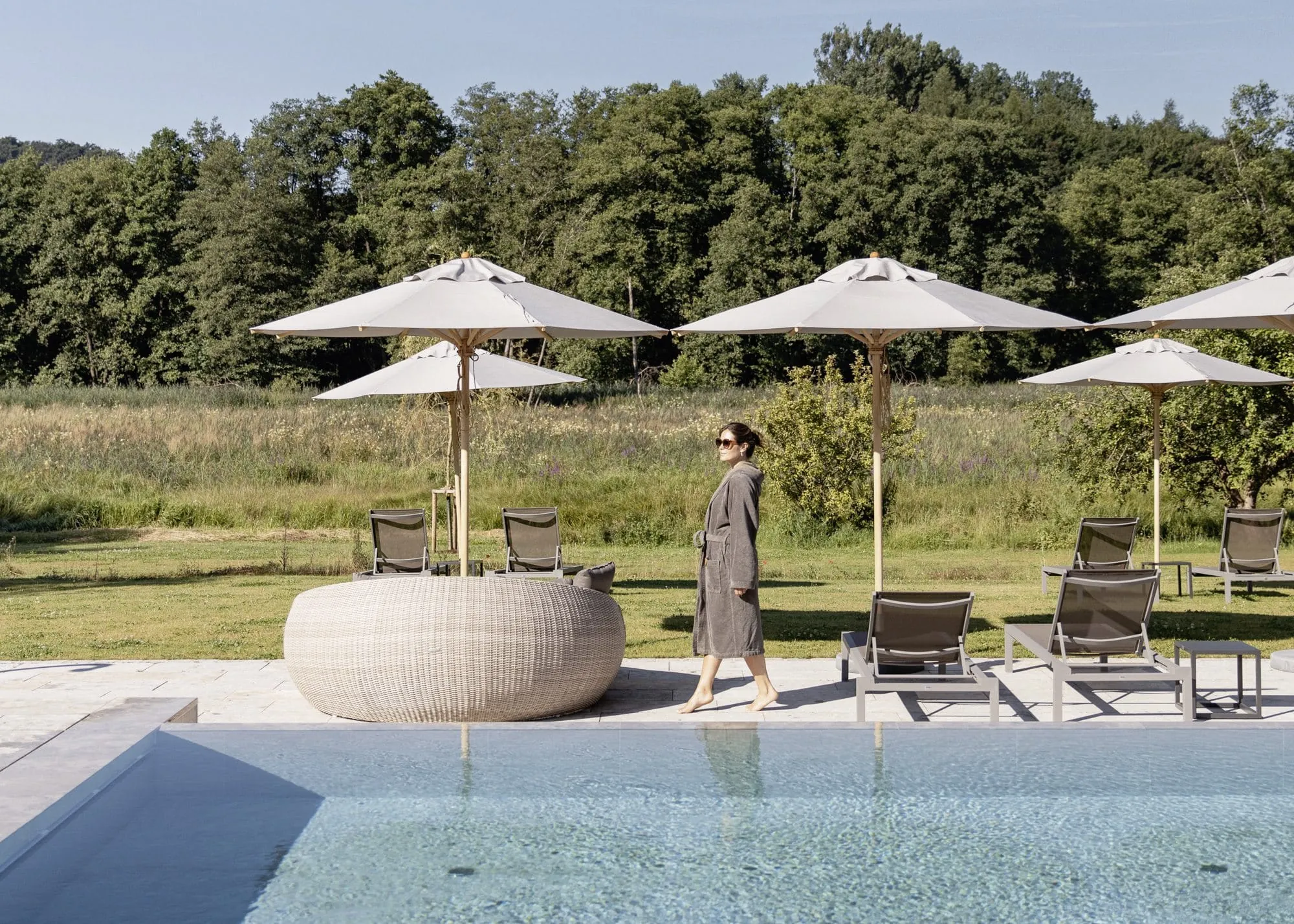 Frau in grauem Bademantel steht am Beckenrand des Outdoorpools des Hotel Winkler Bräu