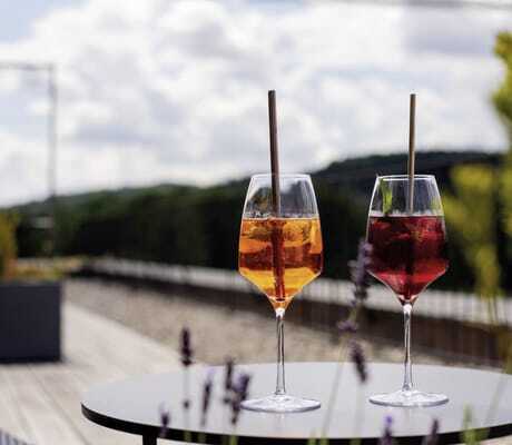 Zwei gefüllte Aperitifgläser, eines orange, das andere rötlich, auf einem runden Tisch auf der Terrasse des Hotel Winkler Bräu