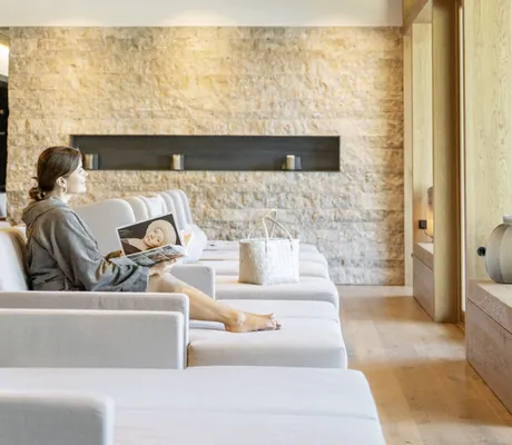 Junge Frau mit einem Buch in der Hand entspannt auf einer hellgrauen Wellnessliege im Ruheraum des Hotel Winkler Bräu