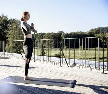 Junge Frau macht eine Yogaübung auf einer Yogamatte auf der Holzterrasse des Hotel Winkler Bräu